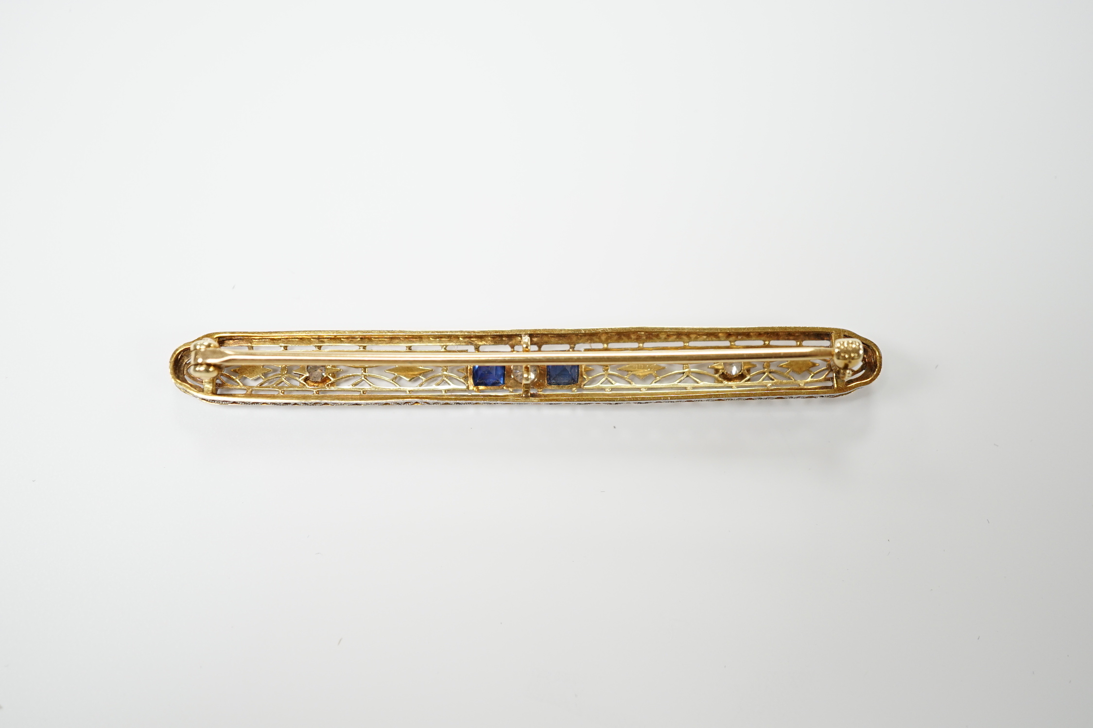 A Belle Époque style pierced 14k, sapphire and diamond cluster set bar brooch, 70mm, gross weight 5.5 grams.